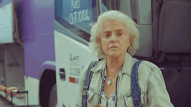 an older woman stands in front of a bus that says no 07.00l