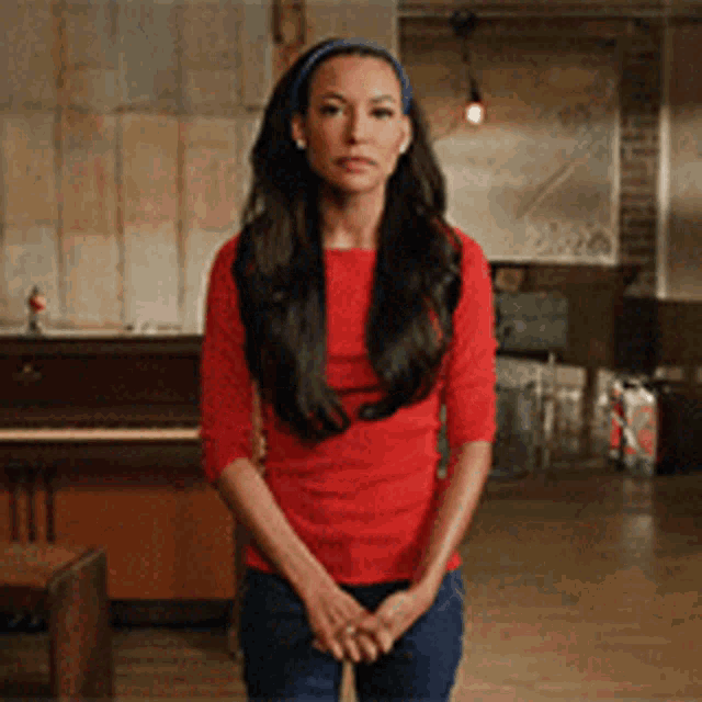 a woman wearing a red shirt and blue headband stands in front of a piano