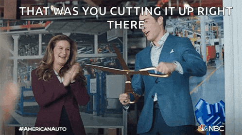 a man is cutting a ribbon with a pair of scissors while a woman applauds behind him .