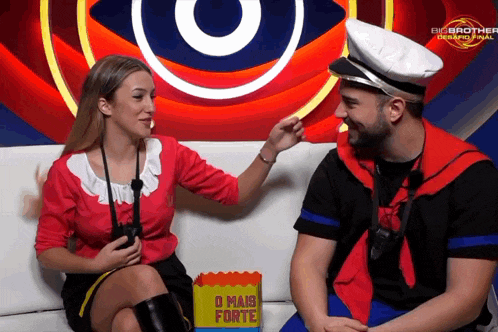 a man and a woman are sitting on a couch in front of a big brother advertisement