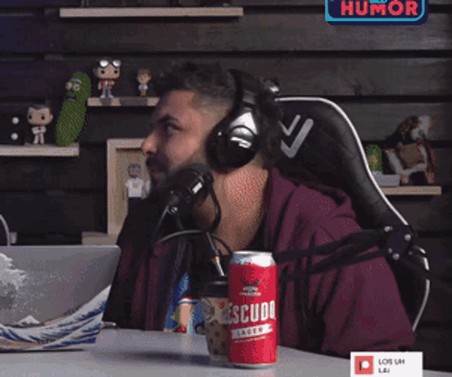 a man wearing headphones talks into a microphone while a can of escudo beer sits on a table