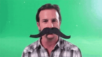 a man in a plaid shirt is wearing a fake mustache on a green screen .