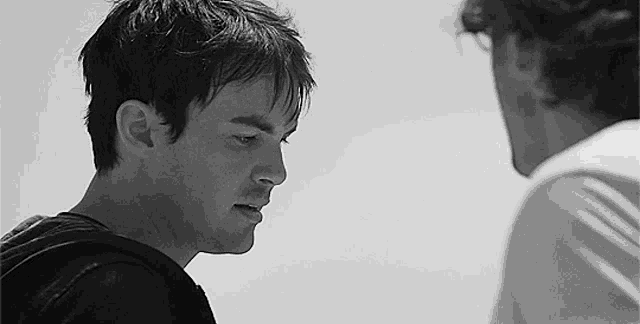 a black and white photo of two men standing next to each other and looking at each other .