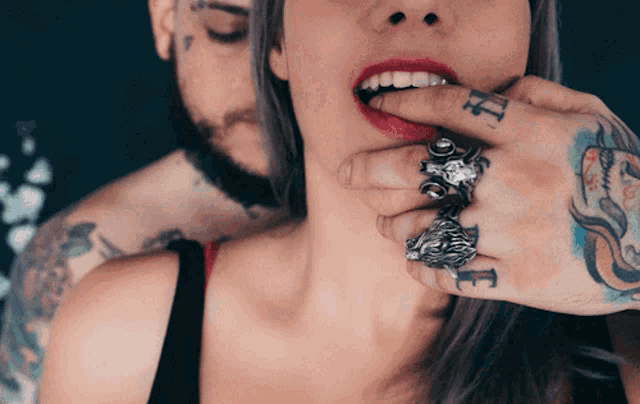 a woman is biting a man 's finger with a tattoo of the letter e on it