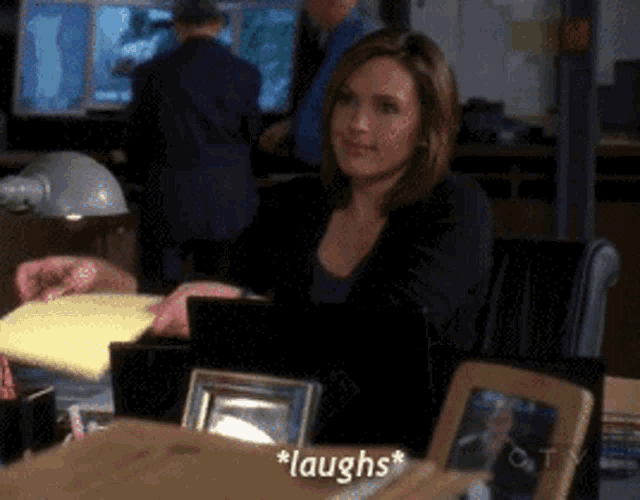 a woman laughs while sitting at a desk with a laptop