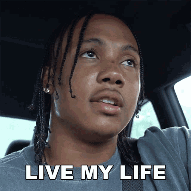 a man in a car says " live my life " in white letters