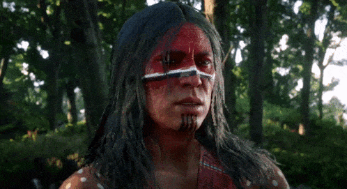 a man with red paint on his face stands in a forest