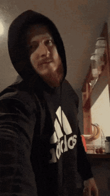 a man wearing a black adidas hoodie takes a picture