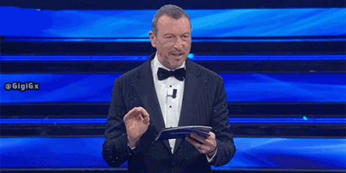 a man in a tuxedo and bow tie is holding a piece of paper in front of a blue background .