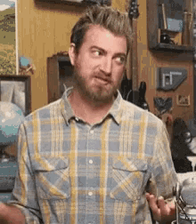 a man with a beard is wearing a plaid shirt and standing in a room .