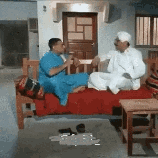 two men are sitting on a bed talking to each other in a room .