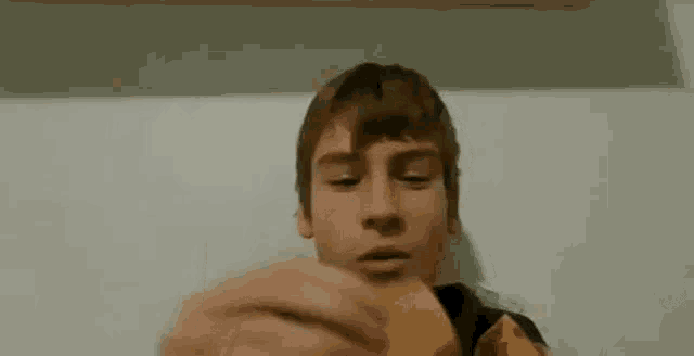 a young boy is eating a piece of pizza while looking at the camera .