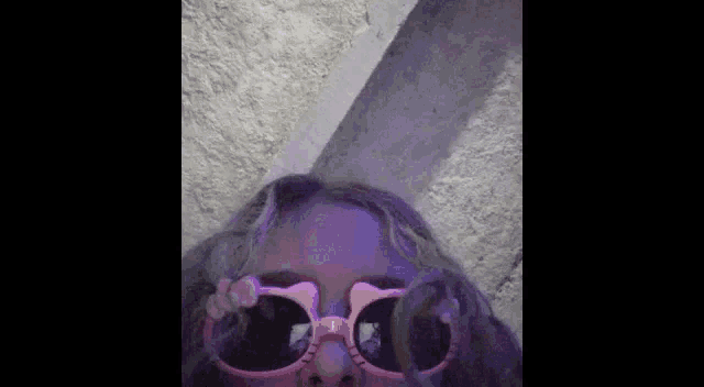 a close up of a person wearing pink sunglasses against a purple background .