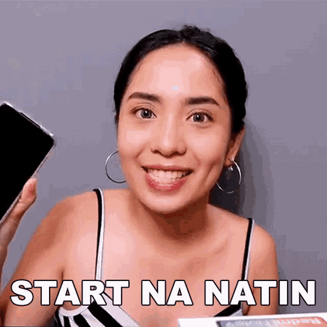 a woman is smiling while holding a cell phone and the words start na natin are on the bottom