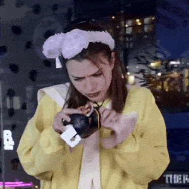 a woman wearing a yellow jacket and a bunny headband is holding a stuffed animal in her hands .