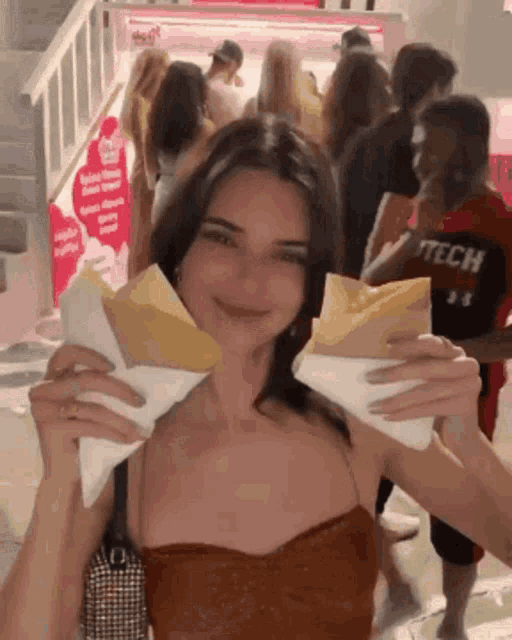 a woman in a tech shirt is holding two crepes in front of a crowd of people