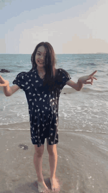 a woman in a blue dress is standing on a beach with her arms outstretched