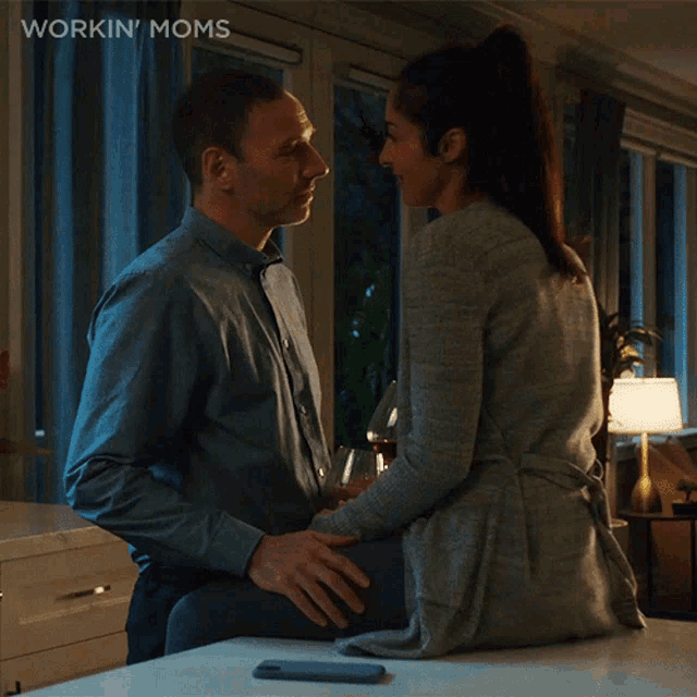 a man and a woman are kissing in front of a sign that says workin ' moms