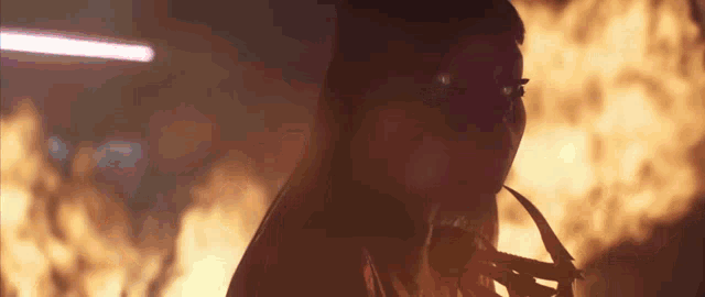 a woman is standing in front of a fire in a dark room with a mask on her face .