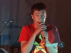 a man wearing a red shirt with a yellow star on it singing into a microphone