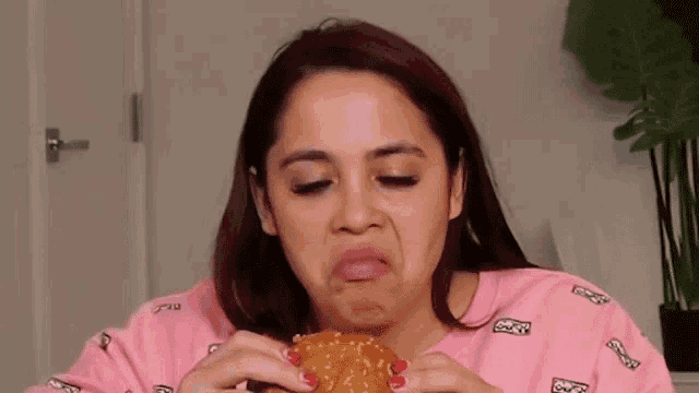 a woman is eating a hamburger and making a face .