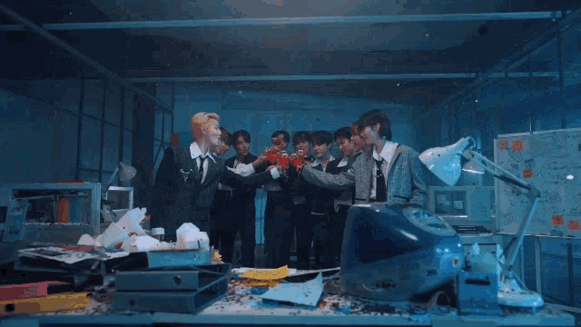 a group of people standing around a messy desk with a blue computer