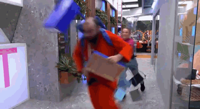 a man in a red jumpsuit is running down a hallway holding a blue bag .
