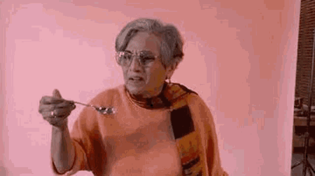 an elderly woman is holding a spoon in her hand against a pink background .