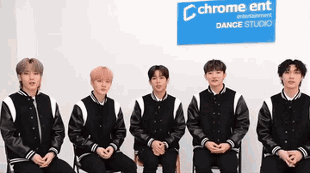 a group of young men are sitting in front of a sign that says chrome ent
