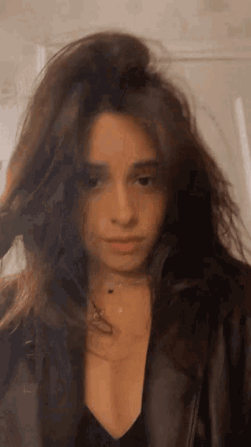 a woman with long dark hair is wearing a black leather jacket and a black top .