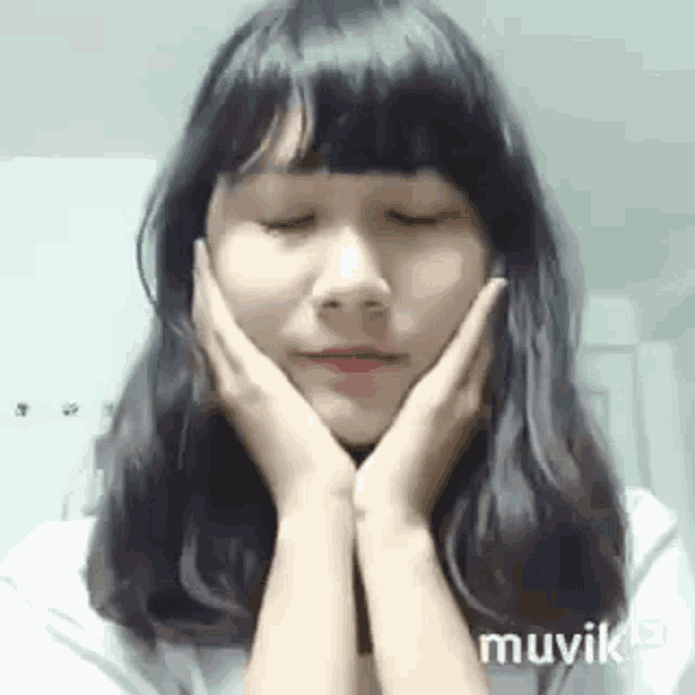 a young woman is holding her face with her hands .
