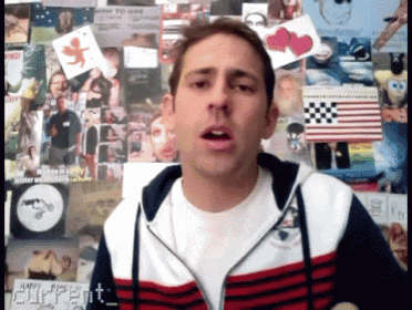 a man in a red white and blue striped jacket stands in front of a wall with pictures on it and a sign that says current