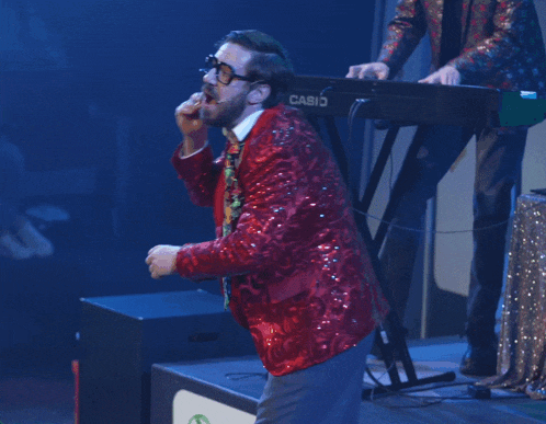 a man in a red sequined jacket is singing into a microphone while playing a casio keyboard