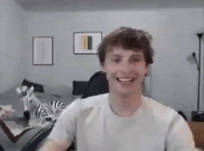 a young man in a white t-shirt is smiling and looking at the camera in a living room .
