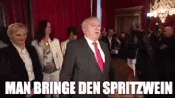 a man in a suit and tie is standing in front of a crowd of people with the caption man bring den spritzwein .