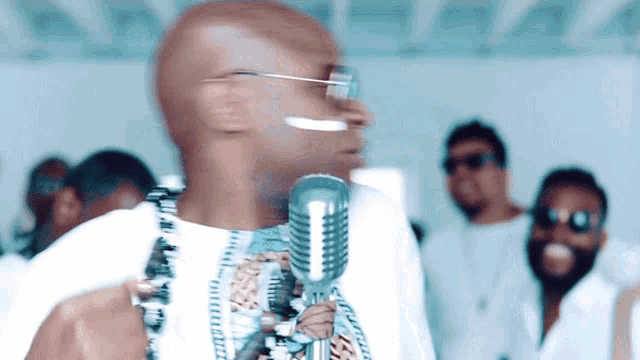 a bald man singing into a microphone in front of a group of men