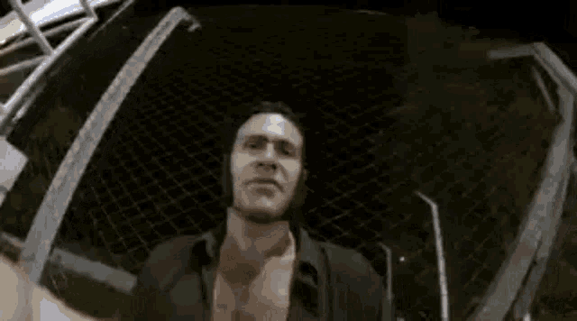 a man is standing in front of a chain link fence at night .