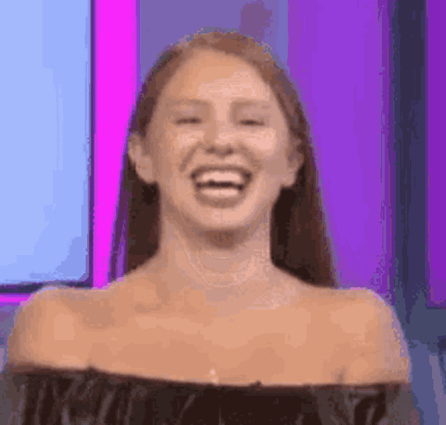 a woman is laughing while standing in front of a pink wall .