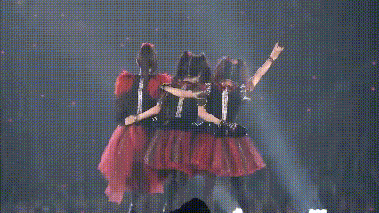 three girls in red dresses are standing on a stage with their arms in the air