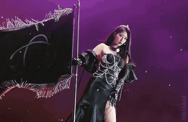 a woman in a black dress is holding a black flag on stage .
