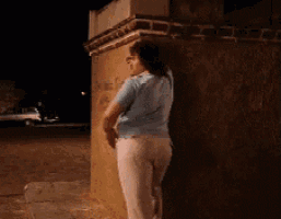 a woman in a blue shirt and white pants is leaning against a wall at night
