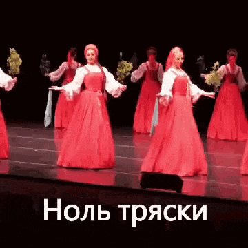 a group of women in red dresses are dancing on a stage in front of a black background .