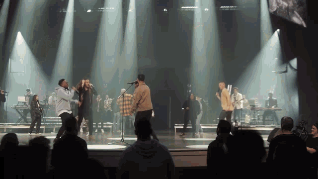 a group of men are singing on a stage with a crowd watching