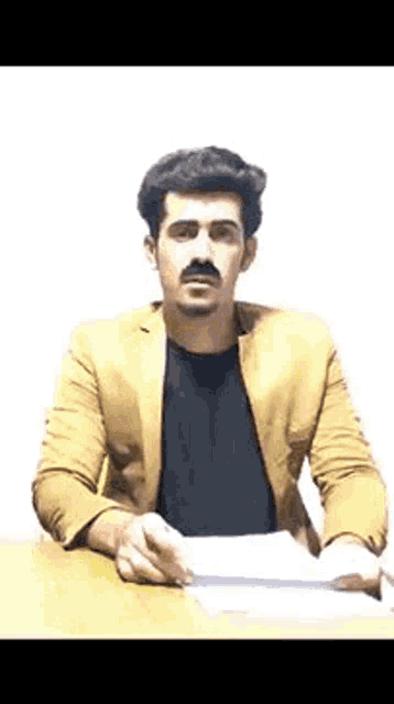 a man with a mustache is sitting at a table with a piece of paper in his hands .