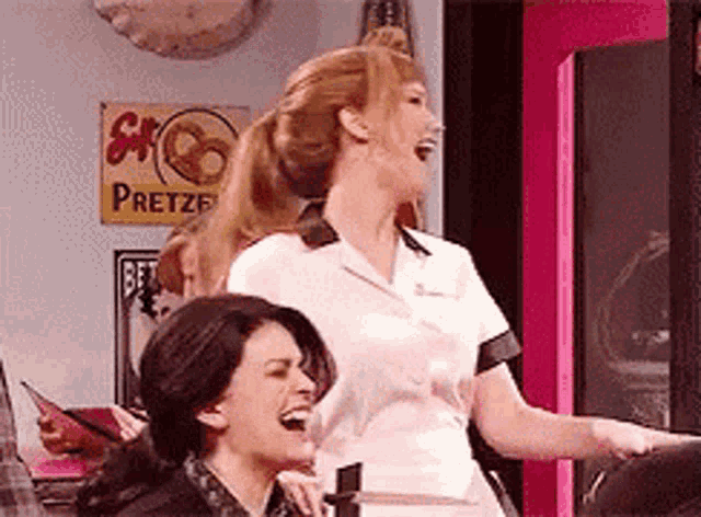 two women are laughing in front of a pretzel sign .