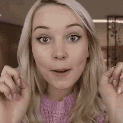 the woman is wearing a pink sweater and making a funny face .