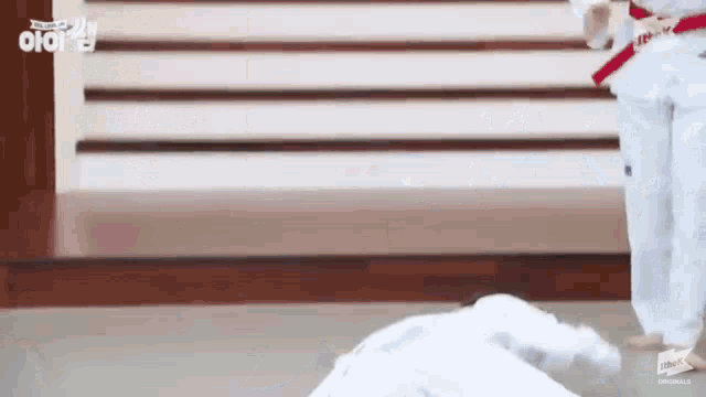 a person in a white karate uniform with a red belt is doing a karate move on the floor .
