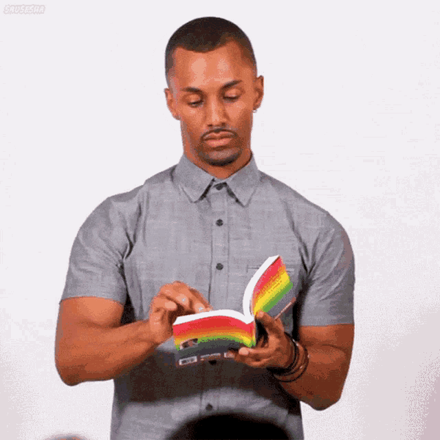 a man in a grey shirt is reading a book with a rainbow colored cover