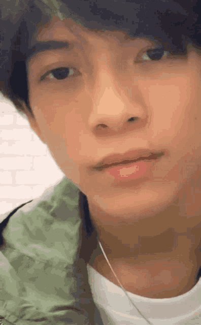 a close up of a young man 's face wearing a green jacket and a white shirt .
