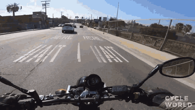 a person riding a motorcycle down a street with the word here painted on the side of the road